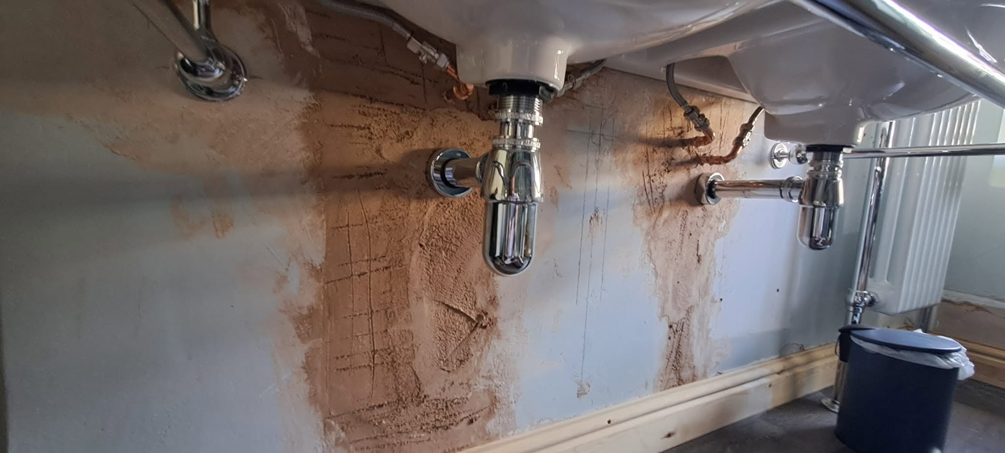 Bathroom wall under two basins with fresh plaster patches before painting