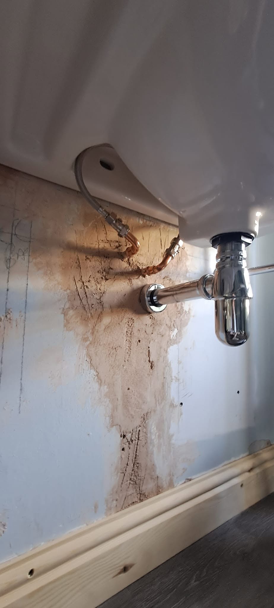 Patched bathroom wall under a basin, ready for painting
