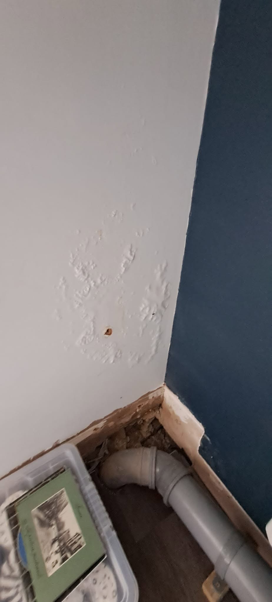 Bathroom corner with the first navy coat going on beside a boxed-in pipe