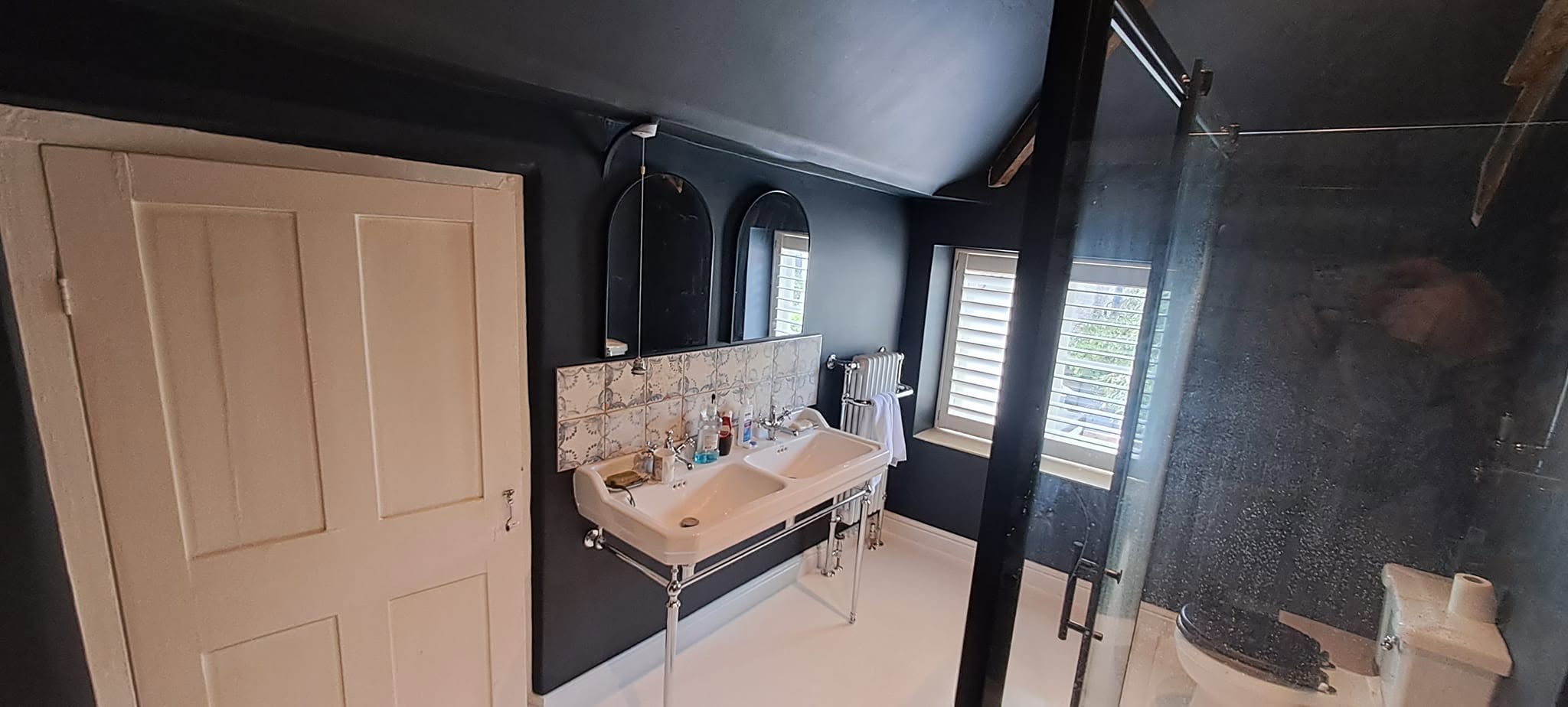 Finished bathroom with navy walls, a cream panelled door and a basin on a stand