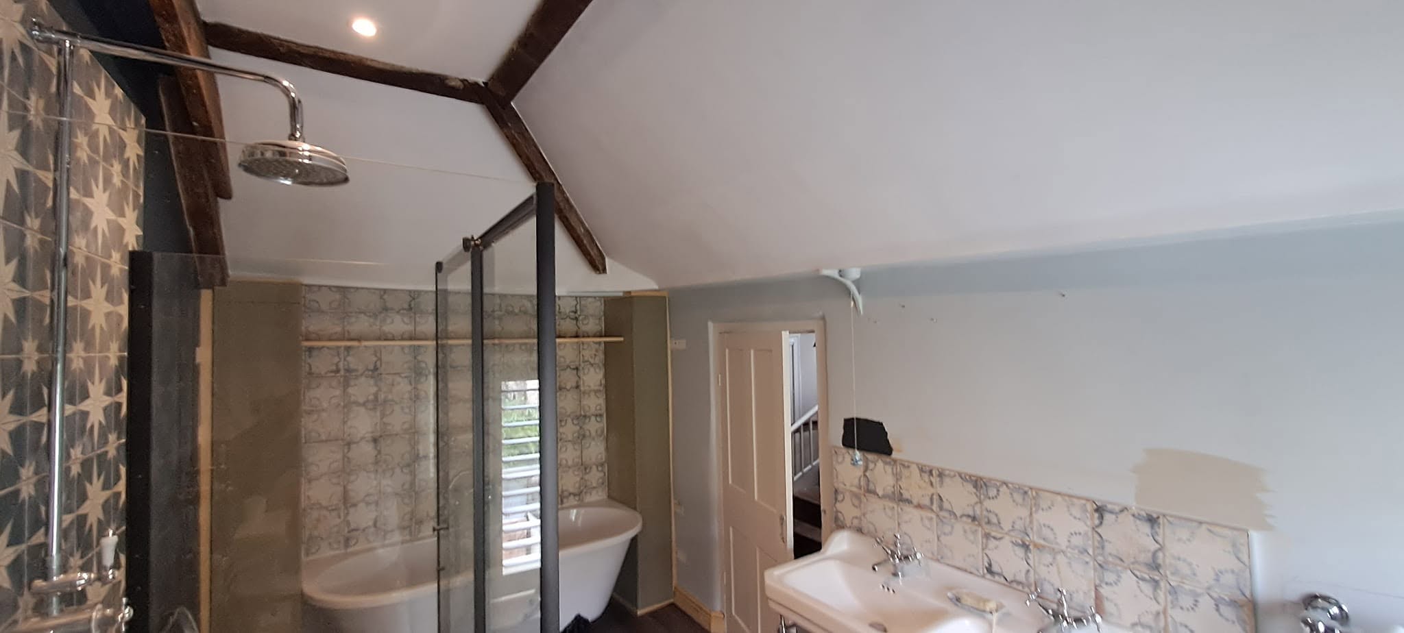 Bathroom under the beams mid-job, with a roll-top bath and pale walls being prepared