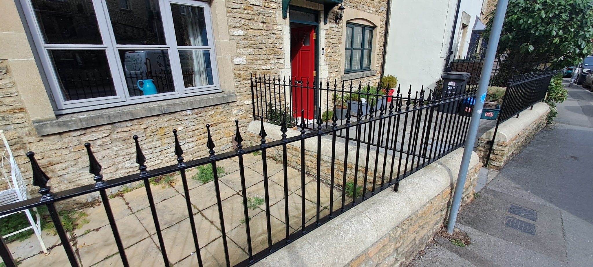 Stone cottage with a red front door behind freshly painted black iron railings